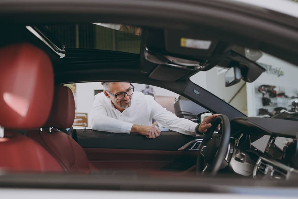 homme en train de regarder l'intérieur d'une voiture dans une concession Autosphère