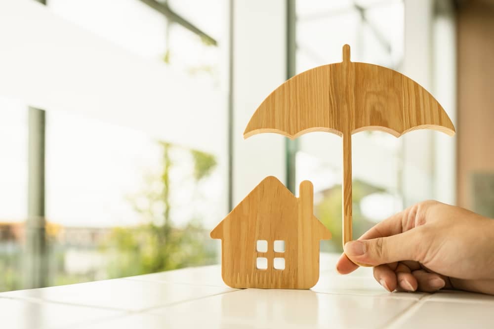 petit parapluie en bois protégeant une maison pour symboliser l'assurance habitation