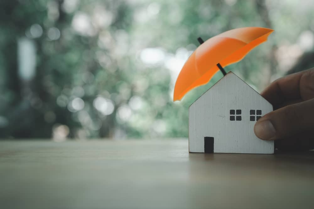 maquette d'une petite maison protégée et assurée par un parapluie orange