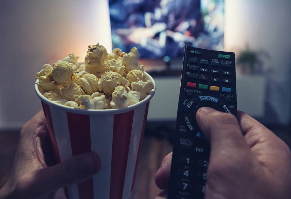 personne avec une télécommande et un pot de popcorns regardant Ciné+