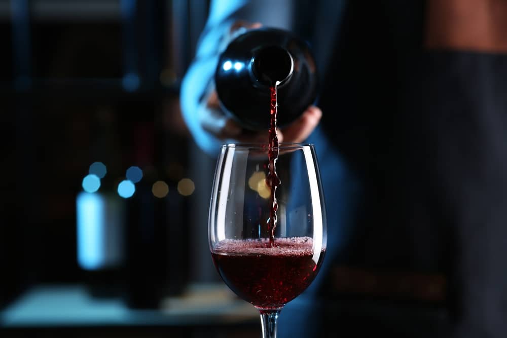 main d'une personne servant du vin rouge dans un verre
