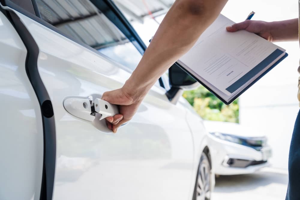 personne près d'une voiture blanche tenant un contrat d'assurance JP Labalette